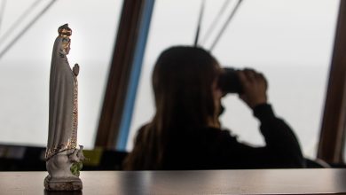 Femme regardant l'horizon sur le pont d'un navire. Statue de la Vierge au premier plan.